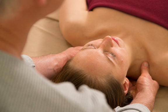 Touchlife Massage - Schulter und Nacken Eine Person erhält eine Massage im Nackenbereich, entspannt auf einer Liege liegend.